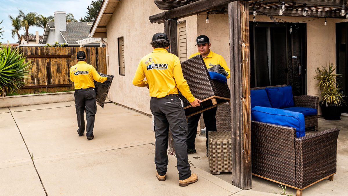Crisan Junk Removal crew carrying patio furniture out of a San Diego backyard